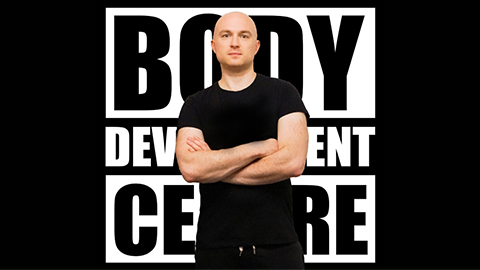 Simon Long wearing a black t-shirt standing in front of a black and white 'Body Development Centre' logo